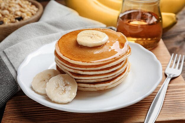 Plate with yummy banana pancakes on wooden board