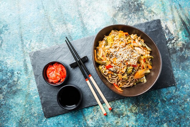 Plate of wok or stir fry noodles with meat and vegetables over blue stone