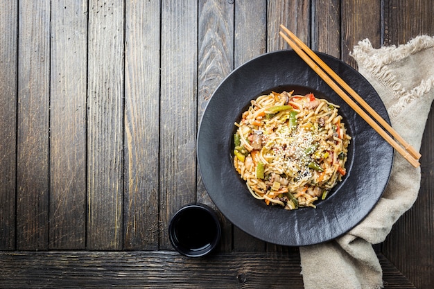 Plate of wok or stir fry noodles with meat and vegetables over wooden