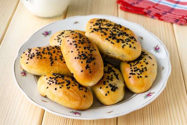 Plate of yeast dough patties with black sesame seeds on wooden background.
