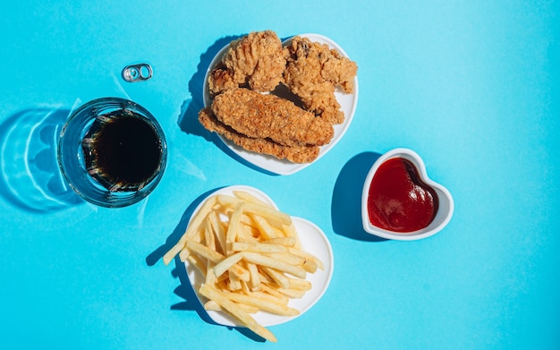 Platen in de vorm van een hart met snacks op een blauwe achtergrond, nuggets, vleugels, strips en friet met ketchup zonlicht harde schaduwen