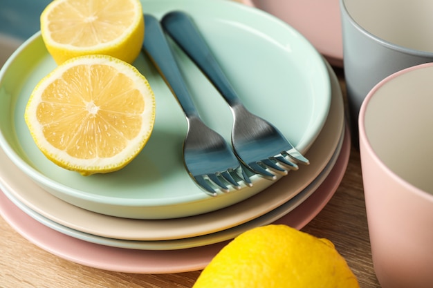 Photo plates and cups with lemons stacked on wooden table, close up