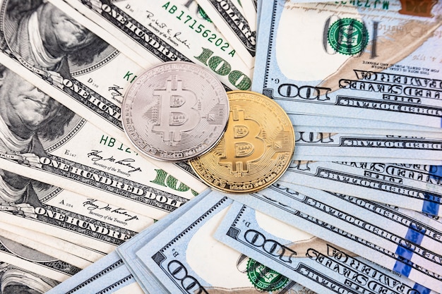 Platinum and gold bitcoin on the background of one hundred dollar bills
