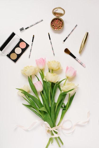 Platliggend bovenaanzicht tafel bureauframe Vrouwelijke blogger bureauwerkruimte met cosmetica lippenstift en tulp bloemen op witte achtergrond