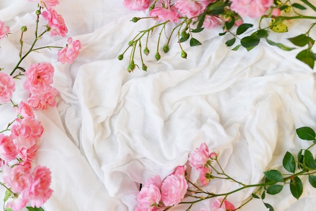 Platliggend frame met roze rozen, takken, bladeren op witte textielachtergrond.