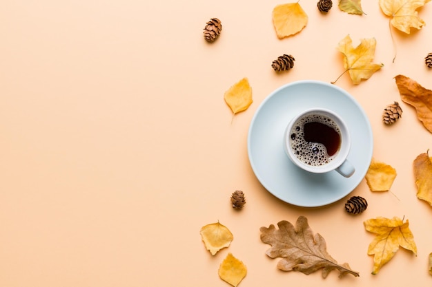 Platliggende compositie met kleurrijke herfstkop koffie en bladeren op een bovenaanzicht in kleur als achtergrond