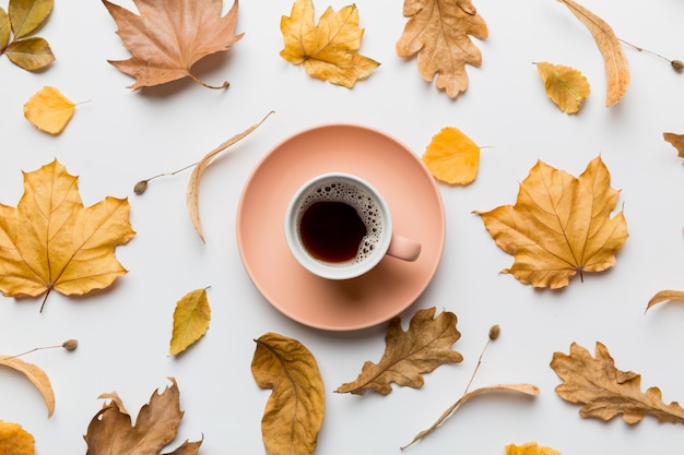 Platliggende compositie met kleurrijke herfstkop koffie en bladeren op een bovenaanzicht in kleur als achtergrond