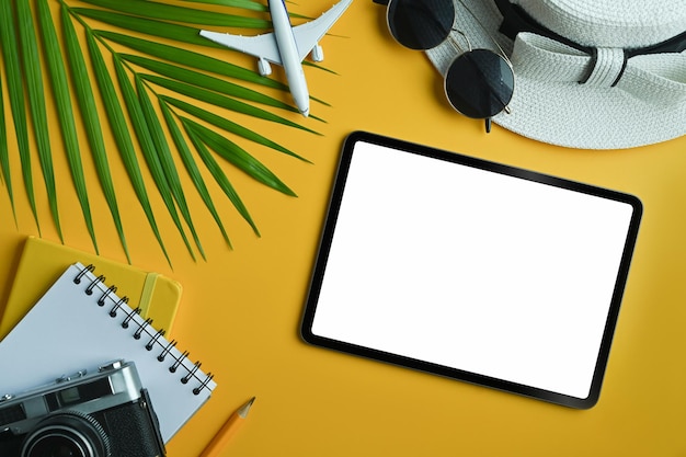 Platliggende digitale tablet met leeg scherm en reizigersaccessoires op gele achtergrond Reis zomer- en vakantieconcept
