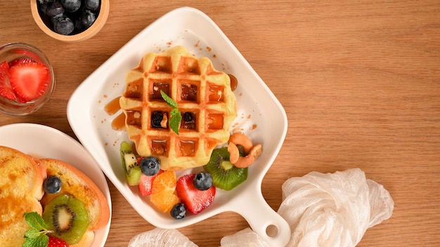 Platliggende, smakelijke wafel met vers fruit en ahornsiroop op houten tafel met kopieerruimte.