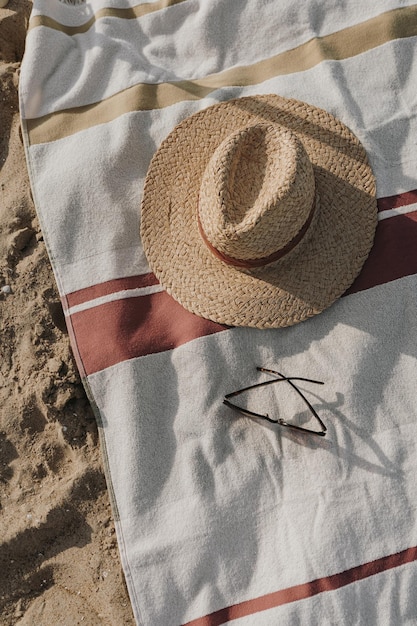 Platliggende vrouwelijke zonnebril strohoed en strandlaken op strandzand Minimale esthetische levensstijl mode blog tijdschrift sociale media Zonnebaden ontspannen chillen op zomervakanties