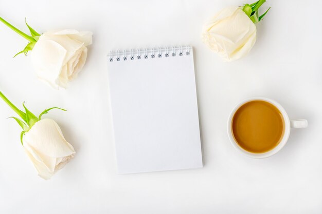 Platte lat bloemen romantische compositie. 'S ochtends koffiemok voor ontbijt, lege notebook met kopie ruimte voor tekst of belettering en witte rozen