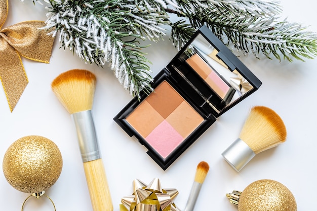 Platte lay compositie met make-up producten en kerst decor op witte achtergrond. Kerst verkoop van schoonheidsproducten concept. blozen op een lichte feestelijke achtergrond met hulst kerst decor bovenaanzicht.