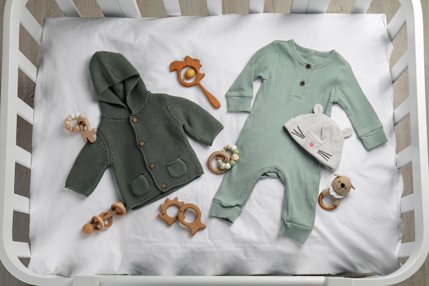 Platte lay compositie met schattige babykleertjes en accessoires op wit laken in wieg