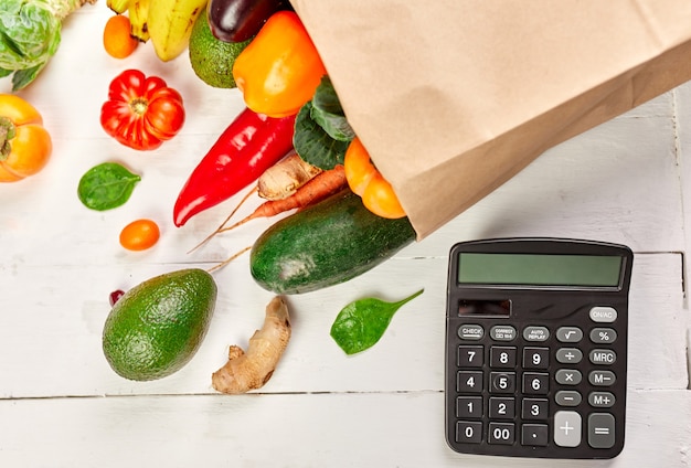 Foto platte papieren boodschappentas met assortiment van verse groenten en fruit en rekenmachine, bio-gezond, biologisch voedsel op witte achtergrond, supermarktstijl, kruidenierswinkel, dieet vegetarisch voedsel.