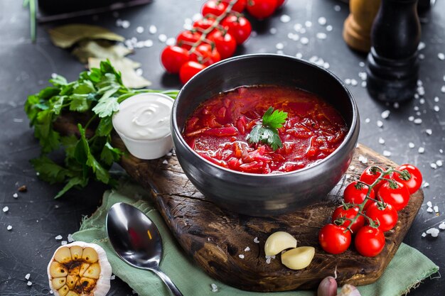 On a platter ukrainian borscht with cabbage, with vegetables, cherry tomatoes, cutlery on a black is