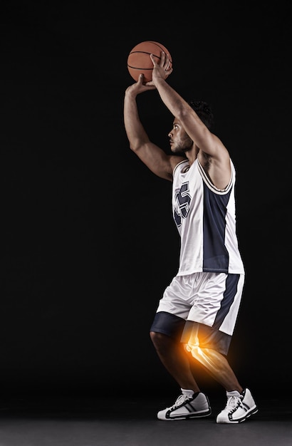 Foto gioca attraverso il dolore scatto in studio di un bel giovane giocatore di basket con un ginocchio infiammato