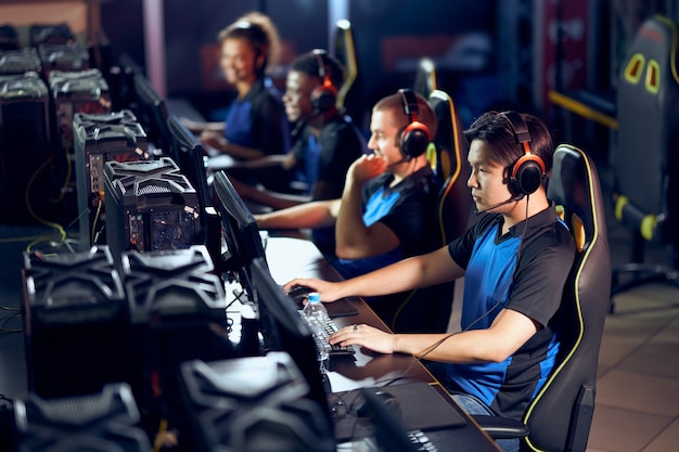 Play to win. Multiracial team of professional cybersport gamers wearing headphones participating in global eSport tournament, playing online video games, side view