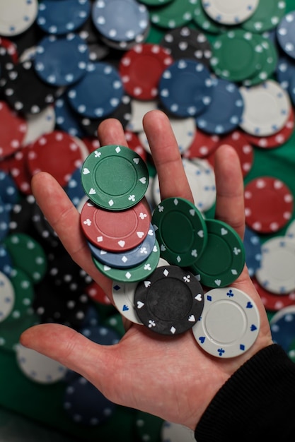 игрок держит покерные фишки. Мужской игрок казино, держащий фишки с фишками для покера на заднем плане.