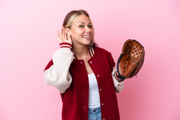 Player Russian woman with baseball glove isolated on pink background listening to something by putting hand on the ear