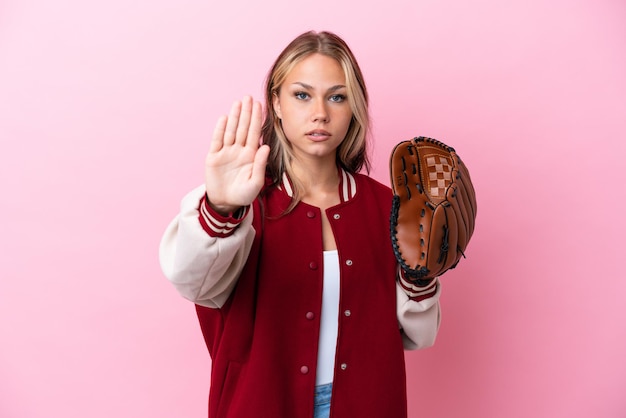 停止ジェスチャーを作るピンクの背景に分離された野球グローブを持つプレーヤーロシアの女性