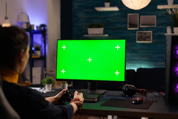 Player using horizontal green screen on computer, playing video games with controller. Woman looking at chroma key with isolated background and mockup template on monitor display.