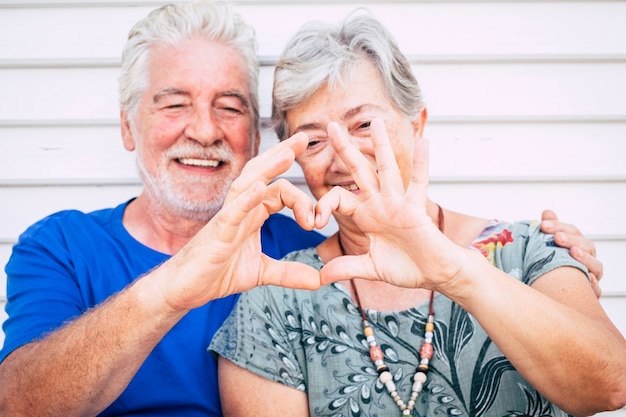 Photo playful beautiful cheerful caucasian adult senior couple enjoying lifestyle toghetner with smile and laugh doing heart with hands. love and partnership forever concept for happy man and woman people