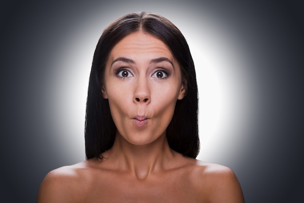 Playful beauty. Portrait of beautiful young shirtless woman staring at camera and grimacing while standing against grey background