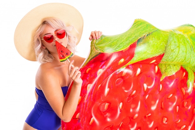 Playful blonde in a blue swimsuit and red sunglasses on a white isolated background