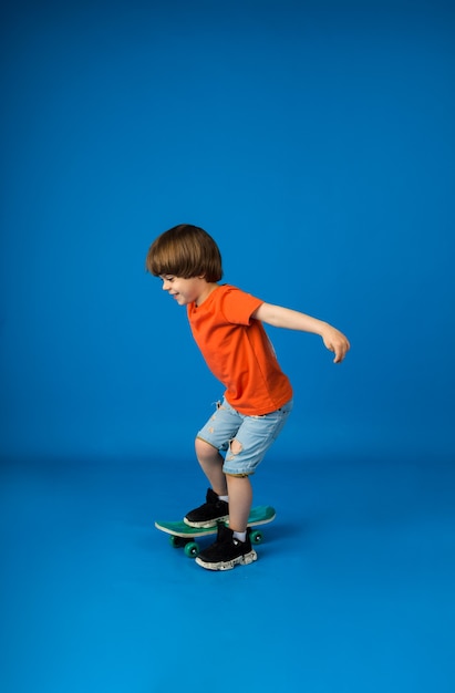 Il ragazzo allegro con i capelli castani cavalca uno skateboard su una superficie blu con un posto per il testo