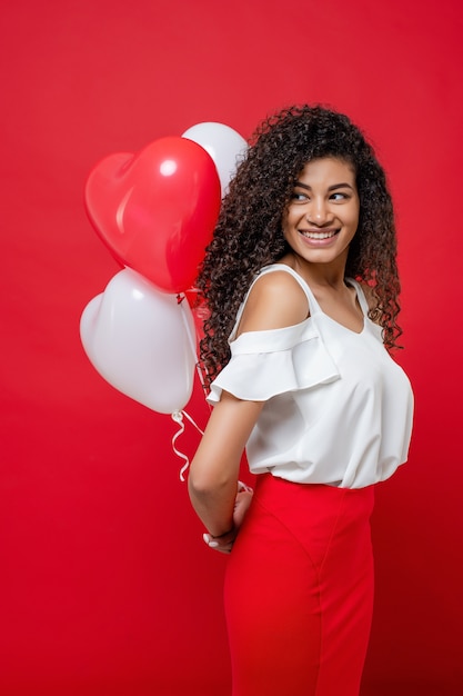 Playful cheerful black woman holding colorful balloons isolated on red