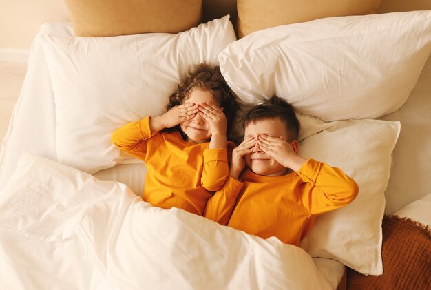 Playful children in yellow pajamas lie on the bed with their eyes closed