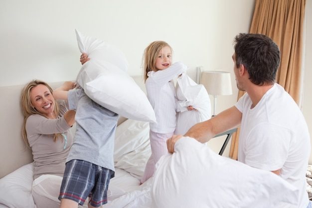 Famiglia giocosa che ha una lotta con i cuscini in camera da letto