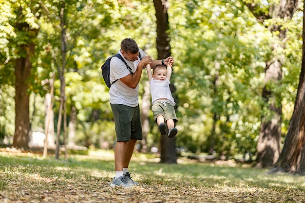 Playful family in the woods Dad holds the boy by the arms and swings him back and forth