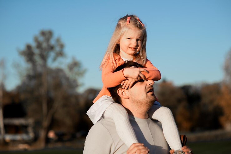 Photo playful father carrying daughter on shoulder during sunset