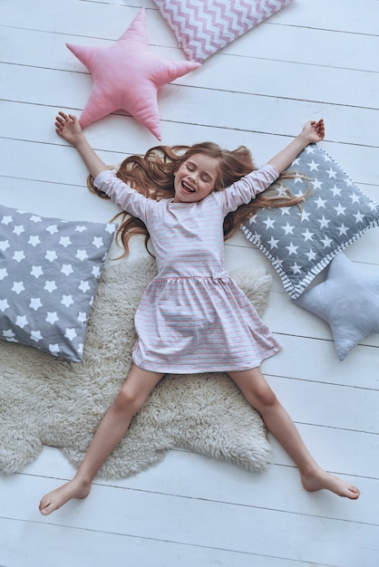 Playful girl. Top view of cute little girl keeping eyes closed and smiling 