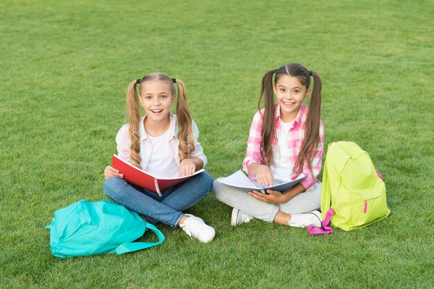 Playful girls literature for girls do homework together find something interesting in book making notes spend free time after school small kid friends relax on grass back to school