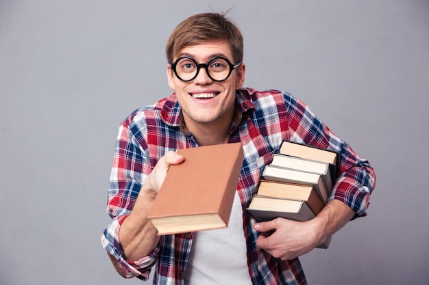 Playful happy young man in checkered shirt and funny round glasses giving youn a book over grey wall