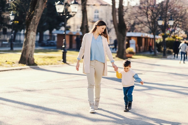 A playful little boy holding hands with his mother in a park on a sunny day