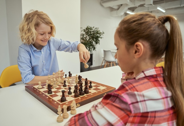 Playful little caucasian boy smiling while making his move playing chess with friend sitting