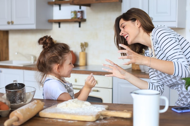 彼女の愛情深い母親と一緒にキッチンで料理をしている遊び心のある少女。