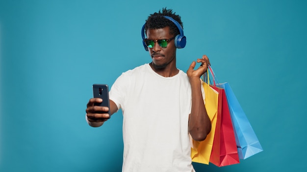 Playful man taking pictures with shopping bags on smartphone
