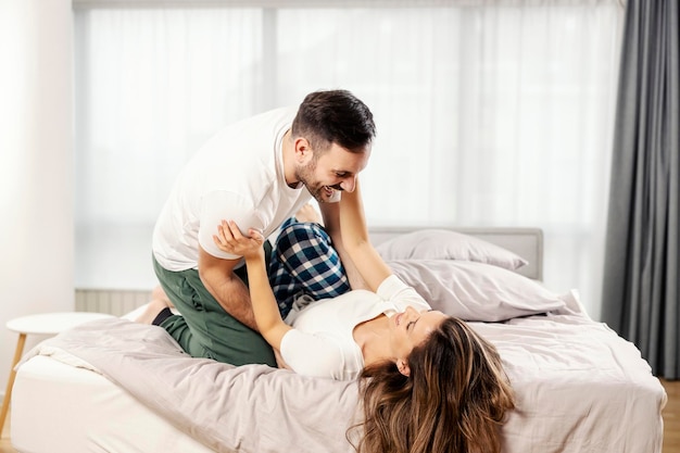 Игривый мужчина щекочет свою жену и играет с ней в постели в спальне