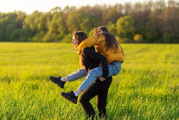 Playful mother giving daughter piggy back ride at green field