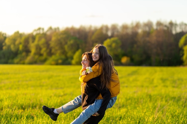 Playful mother giving daughter piggy back ride at green field