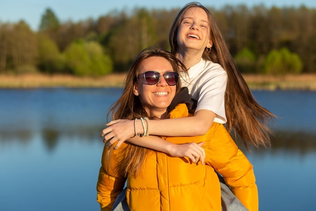 Playful mother giving daughter piggy back ride at spring lake shore