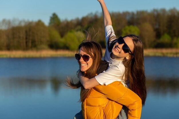 Playful mother giving daughter piggy back ride at spring lake shore