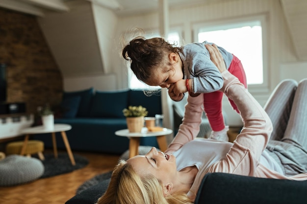 Playful mother spending time with her small daughter and having fun at home.