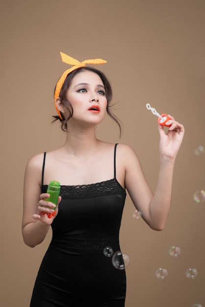 Playful pinup woman blowing party bubbles over yellow background