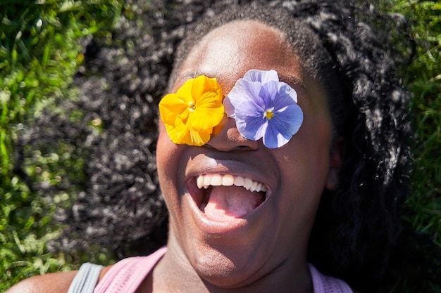 사진 쾌활하고 긍정적인 아프리카계 미국인 여성은 두 개의 꽃으로 눈을 가리고 봄철 신선한 꽃을 즐깁니다.