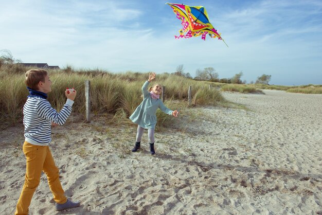 Photo playful sibling flying kite standing on grass against sky